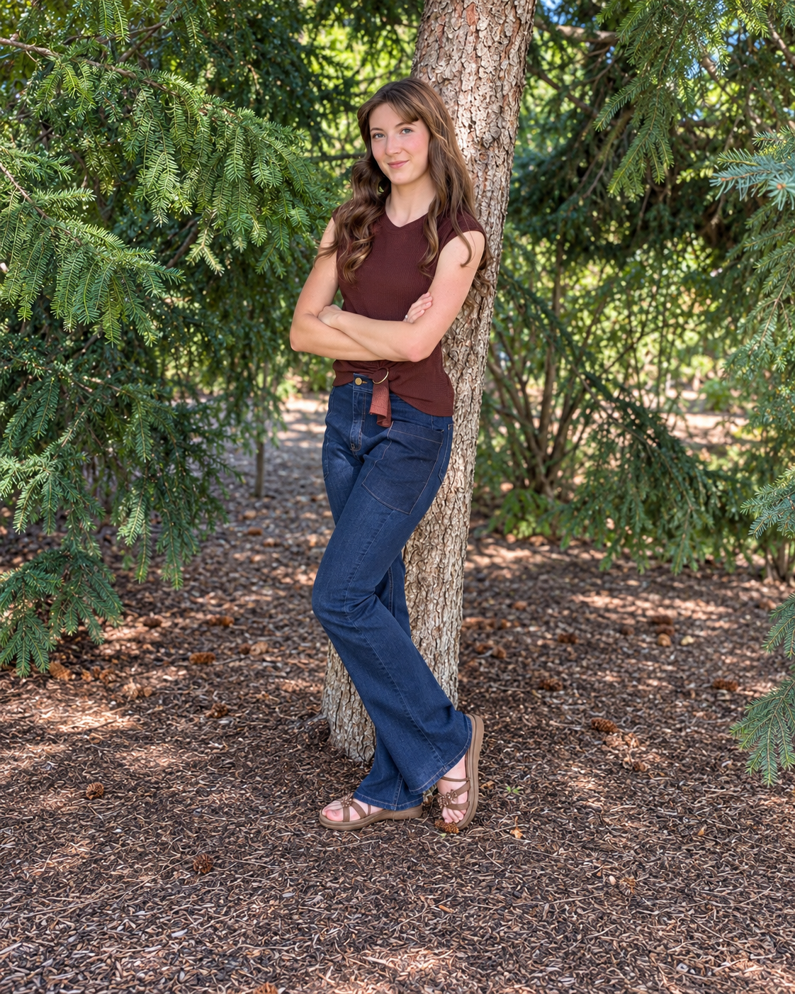 Full-body view of a model wearing dark-wash Roo’s bootcut jeans beside a tree.