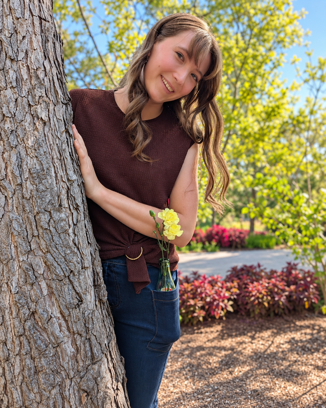 Model wearing Roo's bootcut jeans peaking behind a tree with a bottle of flowers in her pocket