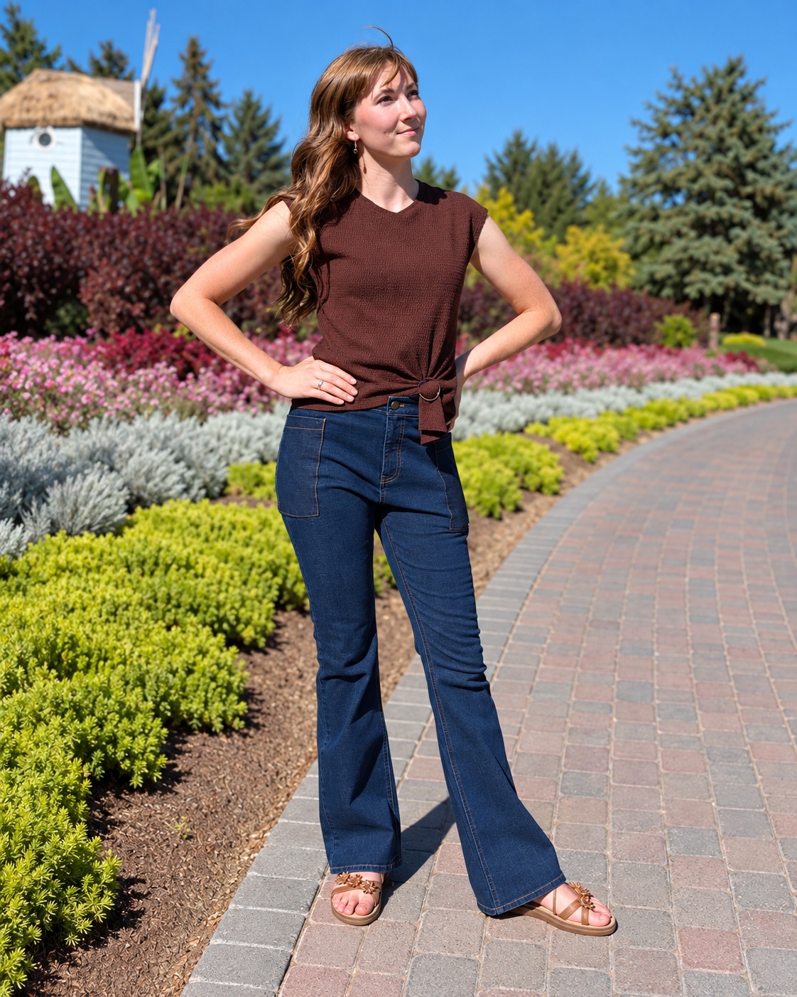 Model wearing dark-wash Roo’s bootcut jeans stands on a garden path, showing the large thigh pocket.