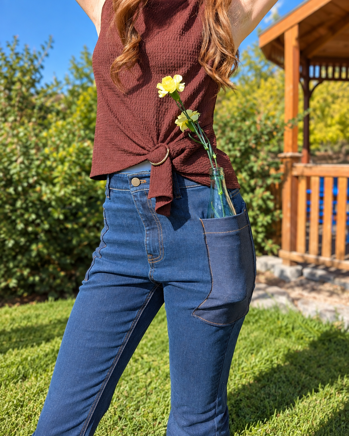 Close-up of dark-wash Roo’s jeans with a glass bottle holding yellow flowers tucked into the oversized thigh pocket.