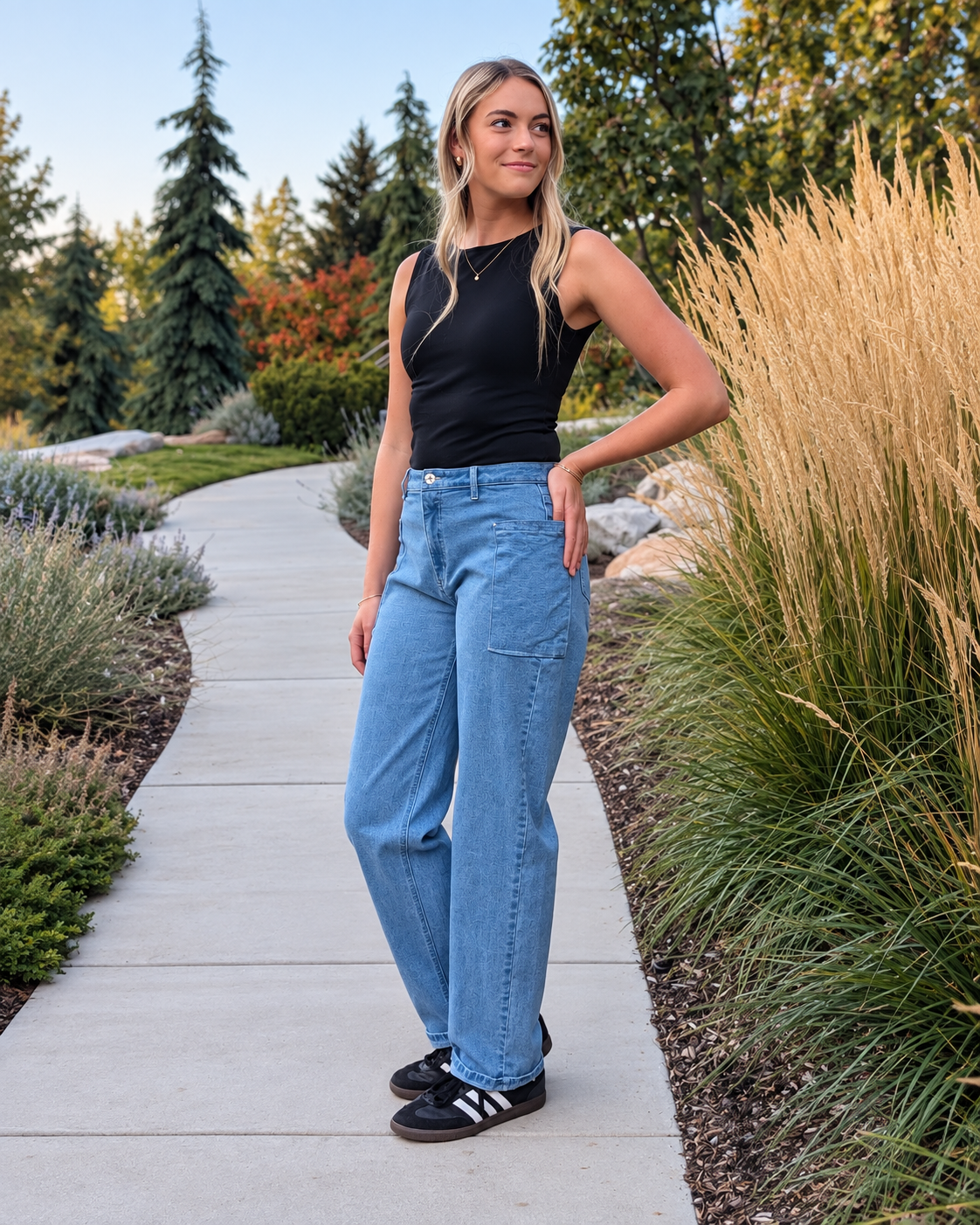 Model wearing light-wash Roo’s jeans stands on a a cement path with one hand on her hip