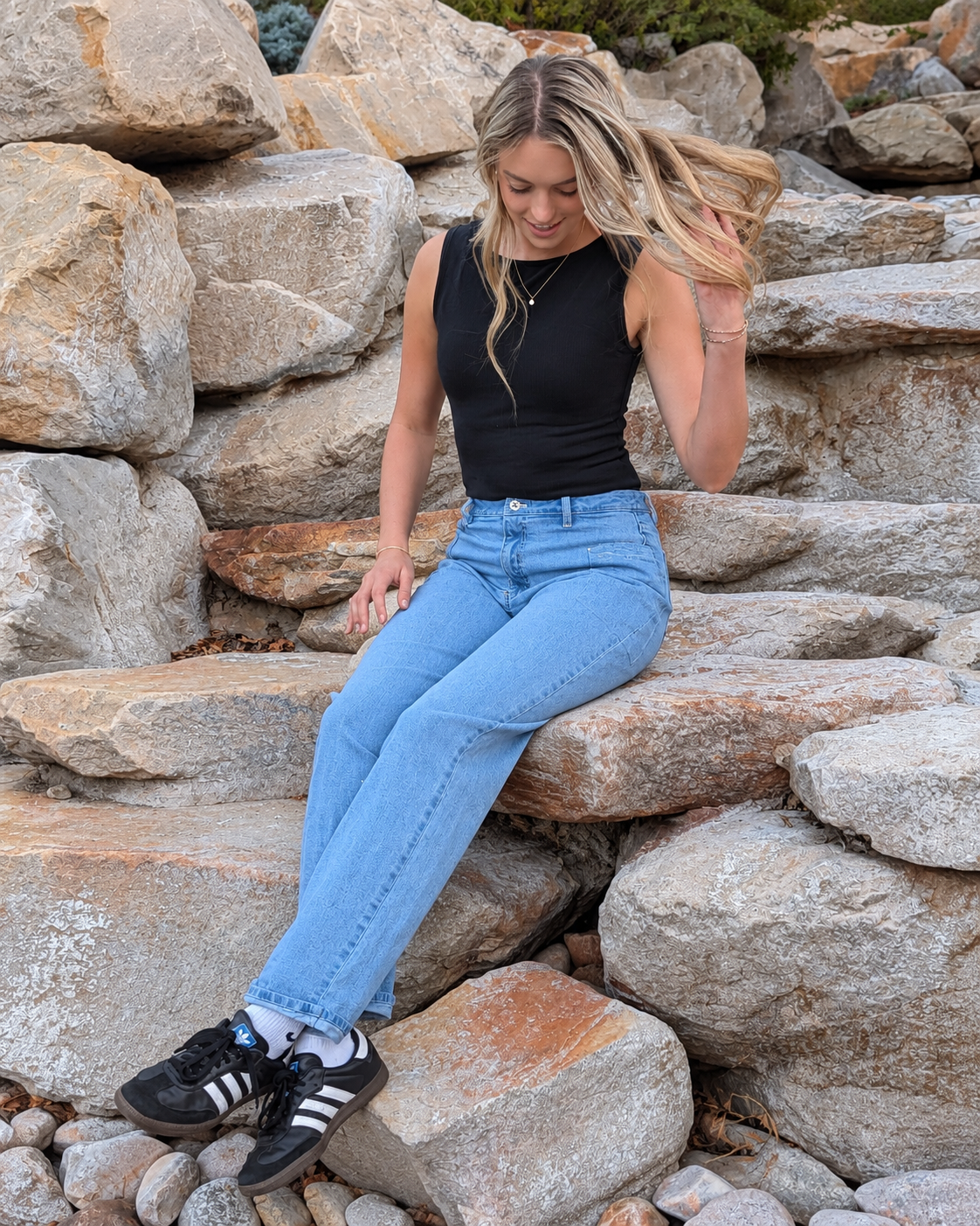 Model wearing light-wash Roo’s jeans sitting on a rock