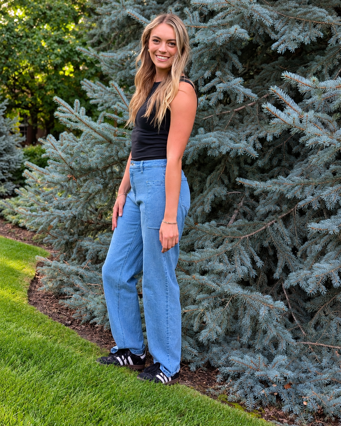 Full-body view of a model wearing light-wash Roo’s jeans on a lawn against a tree.