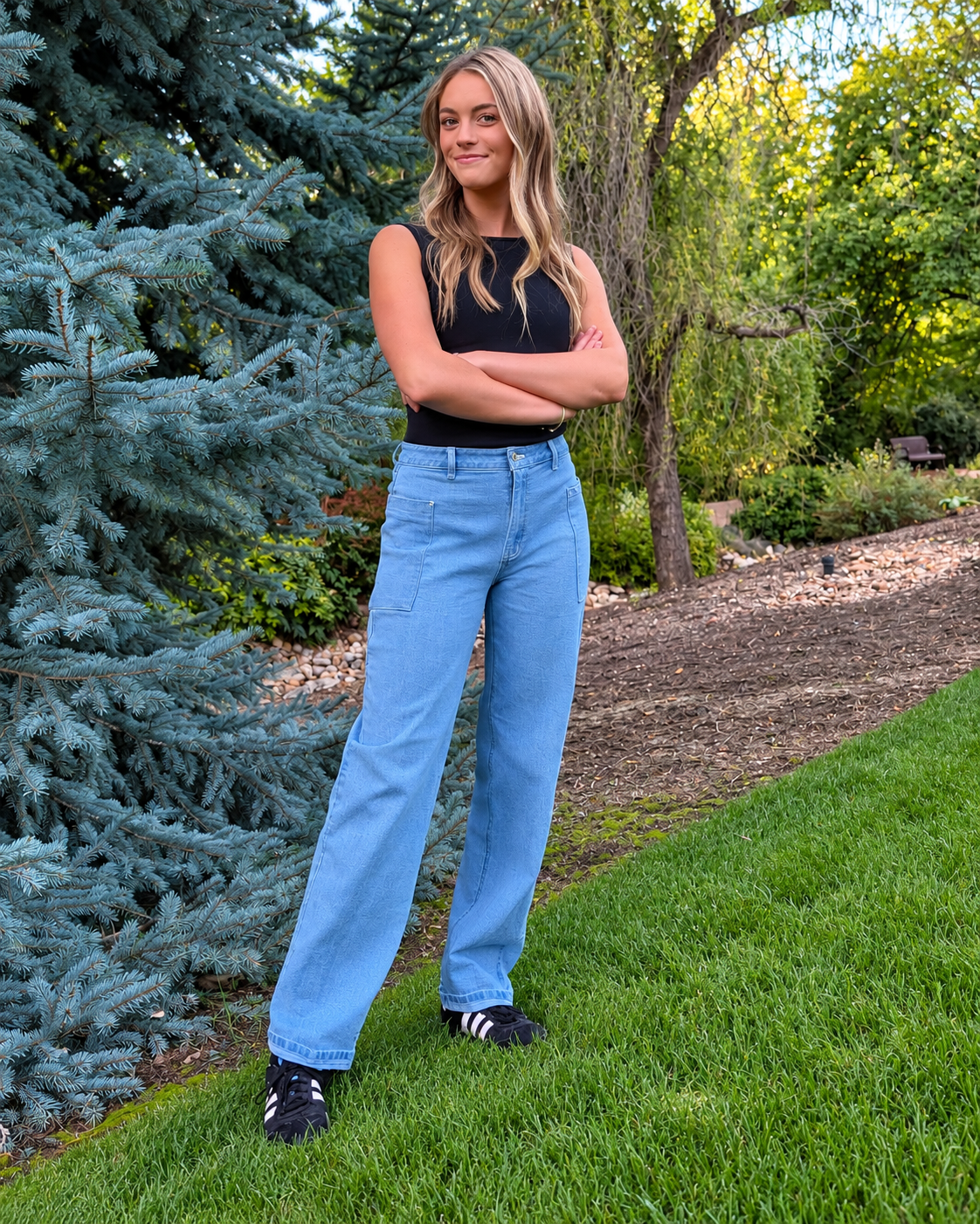 Model wearing light colored Roo's jeans standing on the lawn, with her arms folded.
